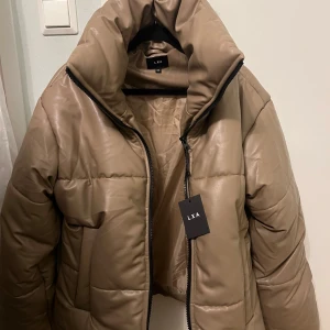 Puffer Jacket LXA - En varm brun/beige vinterjacka från LXA! Aldrig använd så den är i perfekt skick. Storlek XXS men oversize så passar även S-M. Nypris ca 1000 och går ej att köpa längre.