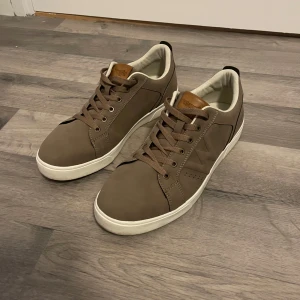 Wrangler skor - Säljer ett par snygga bruna sneakers i nyskick. De har en stilren design med vita sulor och matchande bruna snören. Perfekta för både vardag och fest! Skorna har en bekväm passform och är gjorda i ett slitstarkt material.