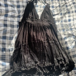 Svart miniklänning med öppen rygg - Säljer denna fina korta svarta klänningen med öppen rygg i storlek S. Den sitter så snyggt på och man kan justera den med snörena runt halsen, ryggen och midjan. 