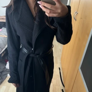 Kappa med skinnskärp - Svart kappa från twist and tango, som helt ny! Helt underbar, knappar plus skärp. Ej äkta skinn. 