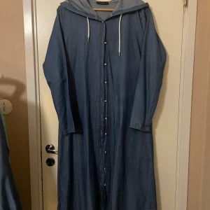 Blå långklänning - Säljer en blå långklänning från Camelya Fashion. Funkar som klänning och som lång öppen kofta Perfekt för en avslappnad dag eller en promenad i stan. Den är i bra skick och har en bekväm passform. Den har även en luva.