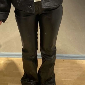 Svarta skinnbyxor - Säljer ett par svarta skinnbyxor i bootcut-stil. De är högmidjade och har en snygg glansig finish som passar perfekt för festliga tillfällen. Byxorna är i nyskick och ger en cool och edgy look. Perfekta för höst och vinter! ända defekten är längst ner på byxorna skriv för bilder! 