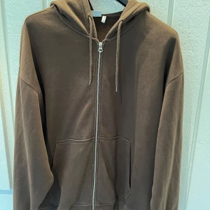 Brun hoodie från Weekday - Säljer en brun hoodie från Weekday i storlek L. Den har en dragkedja framtill och en mysig huva med snören. Perfekt för höst och vinter, och den är i bra skick. Superbekväm och stilren design som passar till det mesta. Skick: 9/10.