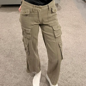 Mörka cargobyxor - Säljer ett par mörka cargobyxor i mycket bra skick. De har flera praktiska fickor med knappar och en loose passform som ger en avslappnad stil. Perfekta för höst och vår. Byxorna är midwaist och gjorda i ett slitstarkt material.