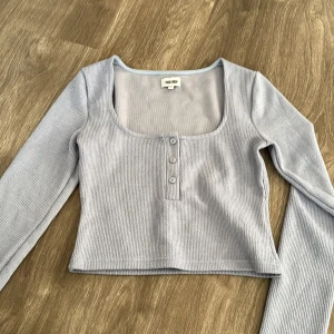 ribbad topp  - Säljer en superfin ljusblå/ljuslila ribbad topp från Bubbelroom. Den har en snygg fyrkantig urringning och tre knappar framtill. Perfekt för både vardag och fest! Toppen är i mycket bra skick och har långa ärmar.