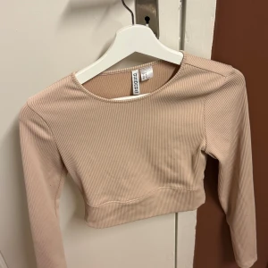 Beige ribbad långärmad topp från H&M  - Säljer en snygg beige ribbad topp från H&M  i storlek M. Toppen har långa ärmar och en croppad passform, perfekt för både vardag och fest. Den är i mycket bra skick och passar utmärkt till höst- och våroutfits.