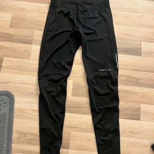 Svarta träningsbyxor från Sportline - Säljer ett par svarta träningsbyxor från Sportline i storlek XL. Byxorna är perfekta för träning med sin elastiska midja och funktionella design. De är tillverkade i ett syntetmaterial som andas och ger bra rörelsefrihet. Perfekta för gymmet eller löprundan!