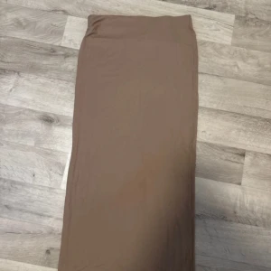 Beige långkjol - Säljer en stilren beige långkjol i bra skick. Perfekt för både vardag och festliga tillfällen. Kjolen har en enkel design utan mönster eller detaljer, vilket gör den lätt att matcha med olika toppar och accessoarer. Ett måste i garderoben för den som gillar minimalistisk stil.