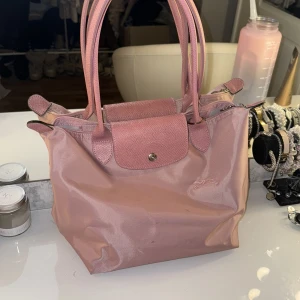 Rosa longchamp väska  - Säljer en superfin longchamp liknande väska. Den har en praktisk dragkedja och en knappdetalj på framsidan. Perfekt för både vardag och fest! 💖köpt på plick så tror inte den är äkta.