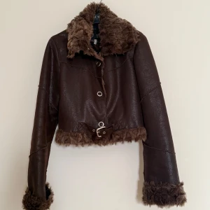 Brun Armani Jeans jacka  med pälsdetaljer - Säljer en snygg brun Armani Jeans jacka med pälsdetaljer på krage, ärmslut och nederkant. Jackan har en croppad stil och knappar framtill. Perfekt för höst och vinter, ger en cool och trendig look. 🧥✨