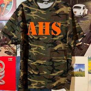 Vintage Camouflage t-shirt med orange text - Säljer en vintage camouflage t-shirt från Port and Company i storlek XL. Den har en fet orange text 'AHS' på framsidan. Inga defekter, dm vid frågor
