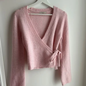 Rosa omlottkofta från Gina Tricot - Superfin rosa omlottkofta från Gina Tricot i mjukt stickat material. Den har en v-ringad design och knytning i sidan som ger en snygg passform. Perfekt för både vår och höst! 💖