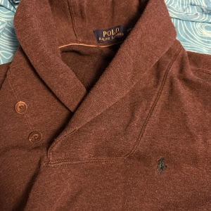 Brun tröja från Ralph Lauren - Säljer en snygg brun tröja från Ralph Lauren i storlek S. Den har en stilren design med en broderad logga på bröstet och knappar vid kragen. Perfekt för höst och vinter, och passar både till vardags och lite finare tillfällen. Superbekväm och i bra skick!