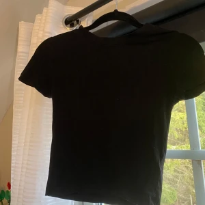 Svart kortärmad topp från H&M - Säljer en enkel och stilren svart kortärmad topp från H&M:s Divided-kollektion i storlek XS. Perfekt basplagg för alla tillfällen. Toppen är i bra skick och använd ett fåtal gånger