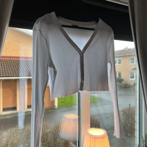 Vit ribbad kofta från Noisy May - Säljer en superfin vit ribbad kofta från Noisy May. Den är croppad med knappar framtill och har långa ärmar. Perfekt för vår och sommar! 🕊️