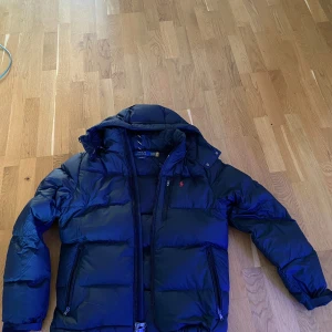 Svart dunjacka från Polo Ralph Lauren - Säljer en snygg svart puffer från Polo Ralph Lauren. Den är perfekt för kalla dagar med sin pufferstil och långa ärmar. Jackan har en dragkedja framtill och är i mycket bra skick. Perfekt för både höst och vinter! Jackan helt ny och oanvänd, storlek S. 