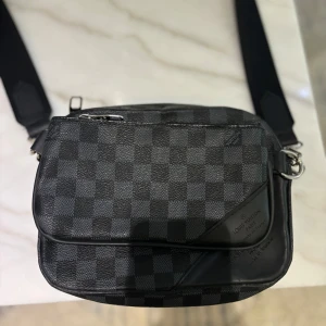 Loui vuitton väska - Snygg och stilren axelväska i svart och grått med klassiskt rutigt mönster. Väskan har en justerbar rem och praktiska dragkedjor har endast använt den några fåtal gånger under sommaren men inte mycket mer än så  1:1K