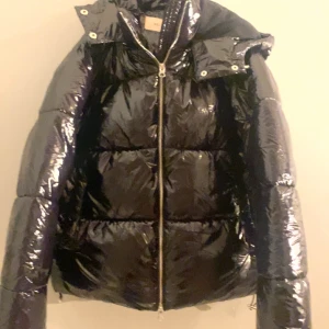 Svart glansig pufferjacka - Säljer den slusålda, trendiga svarta glansiga pufferjackan från nelly helt ny och onvänd. Kan tyvärr inte lämna tillbaks den då jag tappat bort lappen, ordinarie priset är 800 men säljer den för 710 perfekt för vintern! 🤍