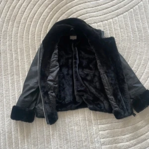Svart skinnjacka från Jofama - Säljer en snygg svart skinnjacka från Jofama i storlek 36. Jackan har en mjuk pälsfodring och dragkedja framtill. Den har långa ärmar med pälsdetaljer vid ärmsluten och en hög krage med spänne. Perfekt för höst och vinter!