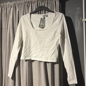 Vit långärmad topp från H&M - Säljer en vit långärmad topp från H&M i nytt skick! Aldrig använt och den har legat i min garderob därav skrynklorna!