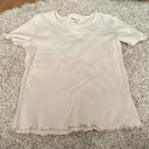 Vit ribbad topp från Ellos - Säljer en superfin vit ribbad topp från Ellos i storlek M. Den har korta ärmar och en söt vågig kant längst ner. Perfekt för både vardag och fest! Toppen är i mycket bra skick och passar till alla säsonger.