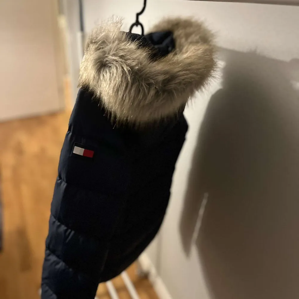 Säljer en snygg mörkblå dunjacka från Tommy Hilfiger. Jackan har en mysig pälskantad huva och dragkedja framtill. Perfekt för kalla vinterdagar! Den är i mycket bra skick och redo för nya äventyr. 🧥❄️. Jackor.