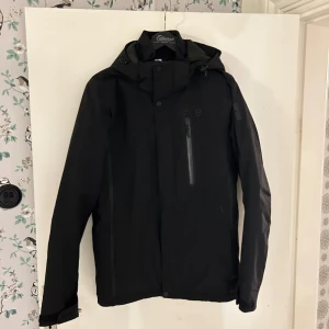 Svart jacka, 8848 Altitude - Säljer en svart jacka från 8848 Altitude i storlek S. Den är perfekt för kyliga dagar med sitt quiltade foder och dragkedja. Jackan har en stilren design med långärmade ärmar och en praktisk huva. Passar perfekt för både höst och vinter!