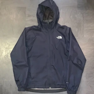 vindjacka The North Face - Säljer en snygg mörkblå vindjacka från The North Face. Perfekt för blåsiga dagar med sin justerbara huva och dragkedja framtill. Jackan har långa ärmar och är i mycket bra skick. Den är både stilren och funktionell, perfekt för höst och vår. 