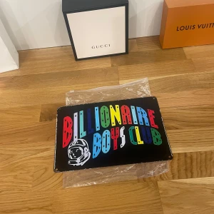 Billionaire Boys Club plåtskylt - Exklusiv Cool plåtskylt från Billionaire Boys Club med färgglad text och astronautmotiv. Perfekt för att ge rummet en unik touch. Skylten är i mycket bra skick och har en stilren baksida i silver. Passar perfekt för den som gillar streetwear och vill ha något extra i inredningen.