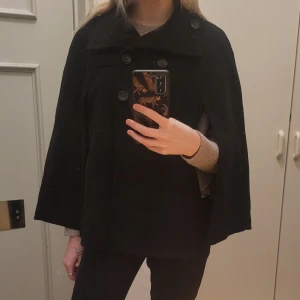 Svart cape med knappar - Säljer en elegant svart cape med dubbelknäppning. Den har en lös passform och är perfekt för höst och vinter. Kappan är långärmad och har en klassisk stil som passar till både vardag och fest. Perfekt för att hålla sig varm och stilren! Sparsamt använd! Kan skicka tydligare bilder vid intresse ❤ storlek XS men passar ända upp till M!
