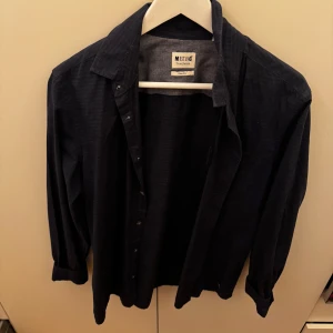skjorta från Mustang - Snygg mörkblå skjorta från Mustang i slim fit. Perfekt för både vardag och fest! Skjortan är långärmad och har knappar hela vägen ner.