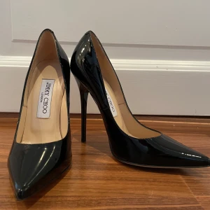 Svarta klackar från Jimmy Choo - Säljer ett par eleganta svarta klackar från Jimmy Choo i storlek 35. Skorna är i lackat skinn med spetsig tå och hög klack, perfekta för festliga tillfällen. De är i mycket bra skick och kommer med originalförpackning.