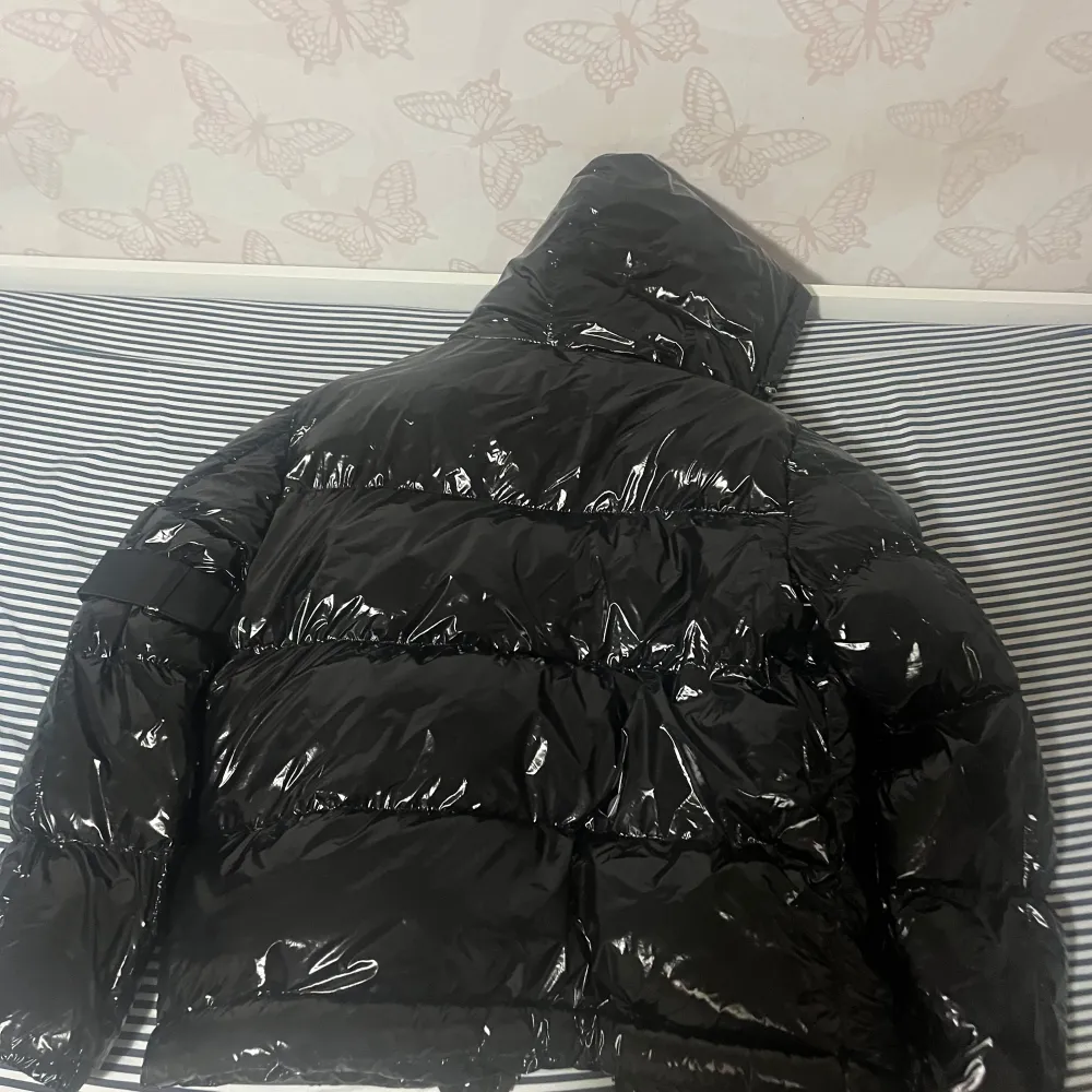 Säljer en snygg svart pufferjacka från Moncler i mycket bra skick. Jackan är perfekt för vintern med sitt blanka polyester-material och har en dragkedja framtill. Den har en cool serietidningsdetalj på insidan och är långärmad med en huva för extra värme. Passar perfekt för kalla dagar!. Jackor.