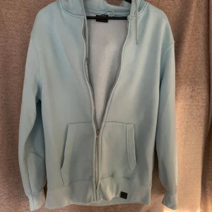 Ljusblå hoodie från Pull&Bear - Säljer en ljusblå hoodie från Pull&Bear i storlek M. Den har en dragkedja framtill och två fickor. Perfekt för en avslappnad stil och passar bra till både vår och höst. Hoodien är i mycket bra skick och supermjuk!