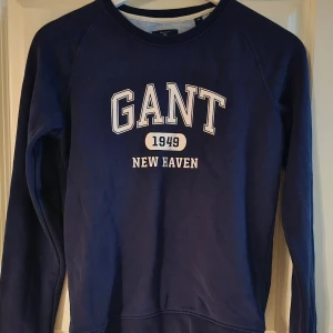 Blå sweatshirt från GANT - Säljer en snygg blå sweatshirt från GANT med tryck 'GANT 1949 NEW HAVEN' på framsidan. Tröjan är i mycket bra skick och har långa ärmar. 