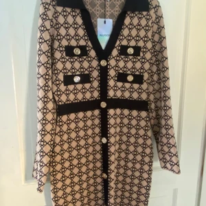 Oanvänd Klänning från RagLady stlk M - Snygg mönstrad klänning från RagLady i beige och svart, med långa ärmar och dekorativa knappar framtill. Perfekt för höst och vinter med sitt eleganta och klassiska mönster och bekväma passform. Klänningen har en klassisk krage och är i nyskick. Stlk M (36/38)