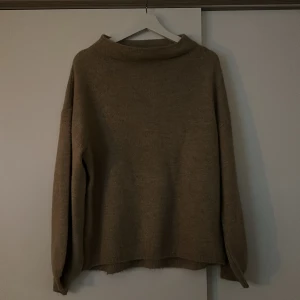 Brun/beige stickad tröja - En brun/beige stickad tröja med en lite högre båtringad hals. Super fin tröja som inte är använd mycket!
