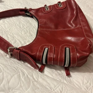 Vinröd axelväska  - Den snyggaste vinröda väskan med bälten på sidorna och dragkedjor, rymmer massor också!!