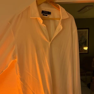 Vit skjorta från Polo Ralph Lauren - Säljer en stilren vit skjorta från Polo Ralph Lauren i slim fit. Skjortan har långa ärmar och klassiska knappar framtill. Perfekt för både formella och avslappnade tillfällen. Den är i mycket bra skick och har den ikoniska broderade loggan långt mer på skjortan. 100% bomull