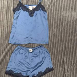 Säljer ett supermysigt blått pyjamasset från H&M i storlek XS. Setet består av ett linne och shorts, båda med vacker spetsdetalj i svart. Materialet är mjukt och skönt, perfekt för en avslappnad kväll hemma. 💙