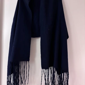 Svart halsduk med fransar från Stockh LM - Säljer en elegant svart halsduk från Stockh LM. Den är i nytt skick och har långa fransar som ger en stilren look. Perfekt för att hålla sig varm under kyliga höst- och vinterdagar. Materialet känns mjukt och lyxigt, vilket gör den både bekväm och snygg att bära.