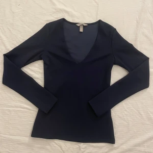 Mörkblå långärmad topp - Snygg mörkblå topp med lång ärm och v-ringning. Perfekt för både vardag och fest. Materialet känns mjukt och stretchigt, vilket ger en bekväm passform. En stilren basplagg som funkar året runt!