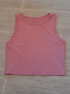 Rosa ribbad linnetopp  - Säljer en rosa croppad linnetopp från SHEIN i storlek XS. Toppen är ribbad med tunna vertikala ränder och är ärmlös med rund halsringning. Materialet är mjukt och stretchigt i polyesterblandning, perfekt för sommardagar. !!endast swish +frakt!!