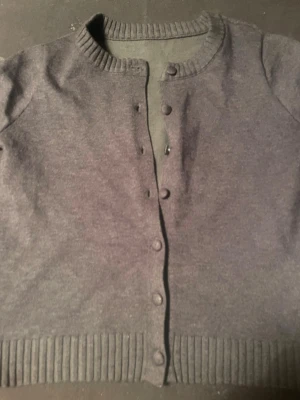 En gullig grå kofta med tyg knappar  - Det här är en kortärmad grå kofta med tyg knappar som är väldigt gullig, vet inte vart den är ifrån men den har andvänts Max 5 gånger och är väldigt fin att ha till vardags och även till lite finare saker 