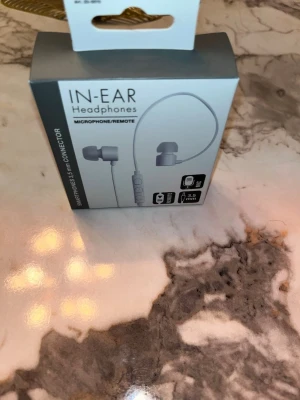 In-Ear Headphones Microphone/Remote 3.5mm - Nya in-ear hörlurar från Biltema med mikrofon och fjärrkontroll. Passar smartphones med 3,5 mm kontakt. Frekvensomfång 20–20000 Hz, impedans 32 Ω, känslighet 90 dB. Kabellängd 1,2 m. Förseglad förpackning, perfekt för samtal och musik.