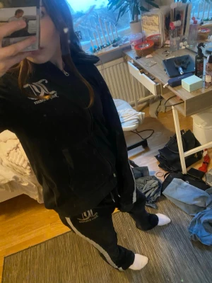 Juicy Couture svart velourväst med glitter - Marin blå set från Juicy Couture med  glittriga silverränder längs ärmarna och benen. Stort Juicy Couture-tryck på ryggen och logga framtill på tröjan och fram till på byxorna. Perfekt för dig som vill ha en ikonisk och trendig look. 500kr för båda delarna men st 250kr