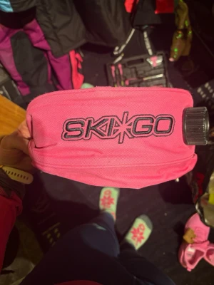 Rosa SKIGO midjeväska med flaska - Säljer en rosa midjeväska från SKIGO, perfekt för längdskidåkning eller träning. Väskan har ett stort fack med dragkedja och inbyggd flaska med skruvlock. Tillverkad i slitstark polyester och justerbart midjeband för bästa passform.