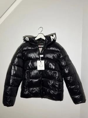 Moncler Jacka - Säljer en unik moncler jacka med svart lite större moncler badge på vänster arm. Det står storlek XL men den sitter som en L-M. Mått på jackan: Längd: 60cm, midians omkrets är 110 cm, innerarms längd: 47cm. Bara att höra av dig vid evuentuella frågor!