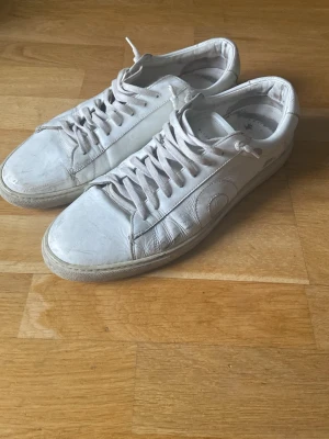 Vita sneakers från Oliver Cabell - Säljer ett par klassiska vita sneakers från Oliver Cabell i skinn. Skorna har rund tå, snörning och diskret logga på hälen. Tidlös design med platt sula och stilrena sömmar. Perfekta till jeans eller shorts för en clean look inför sommaren.