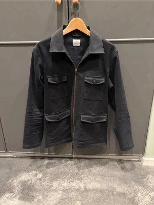 Svart overshirt från John Henric - Säljer en riktigt snygg svart overshirt från John Henric med fyra  fickor framtill och dragkedja. Storleken är S. Mitt pris är 650 för denna overshirt!